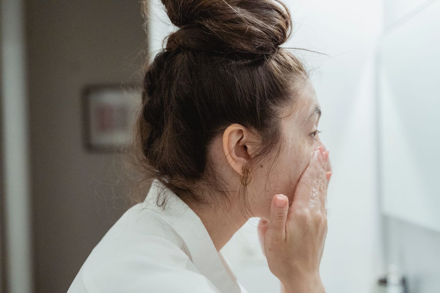 Mujer aplicándose cuidado facial en el baño con luz natural